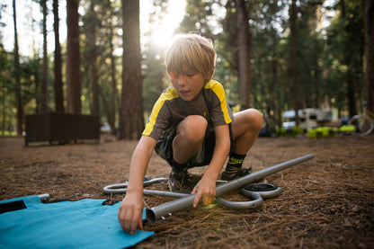 Child setting up camping equipment in a forest