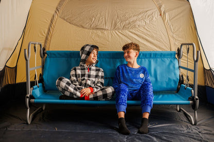 Two children sitting on a blue camping couch in front of a tent.