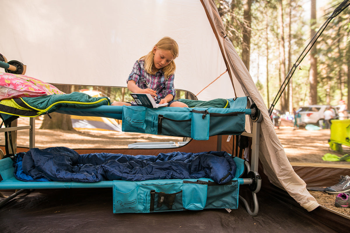 Person setting up a camping bed in a forested area with a tent in the background.